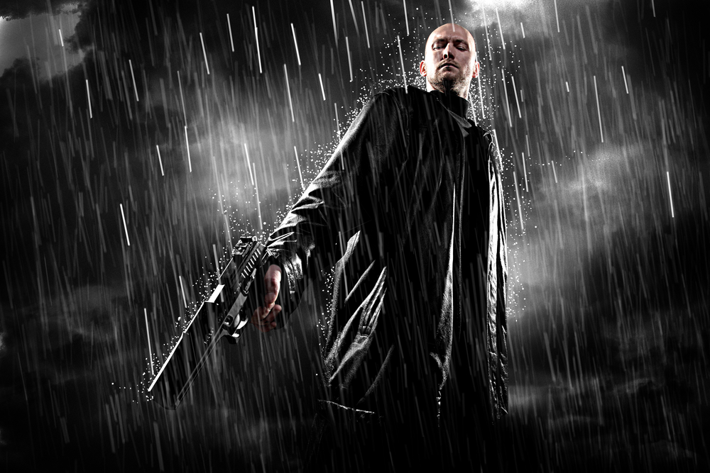 man with a gun, looking down, set against a dark stormy night.